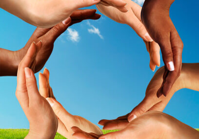 Conceptual peace and cultural diversity symbol of multiracial hands making a circle together on blue sky and green grass background.